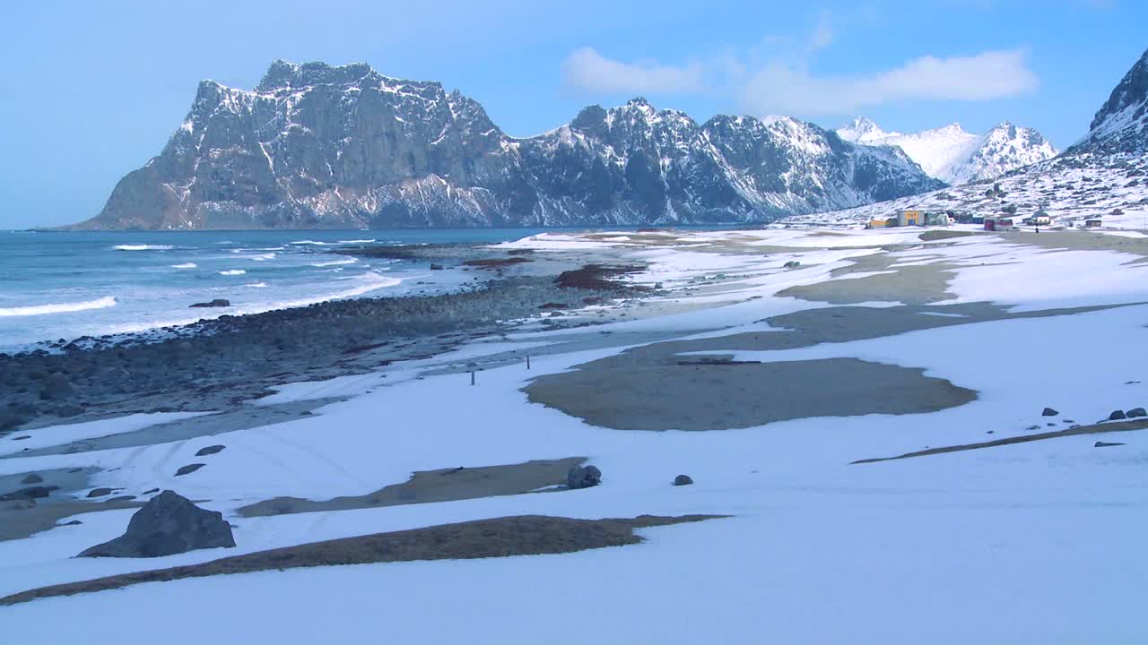 Ondas rolam sobre uma bela praia coberta de neve em meio a fiordes ao norte do Círculo Polar Ártico nas Ilhas Lofoten, Noruega