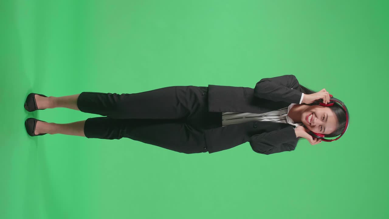 Full Body Of An Asian Business Woman Listening To Music With Headphones And Dancing In The Green Screen Studio