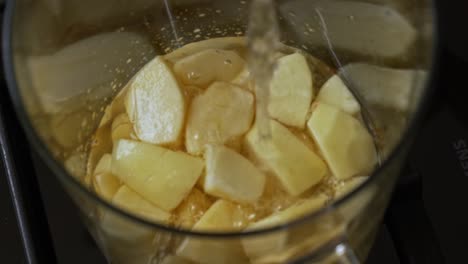 water pours into a glass pitcher of chopped apples on top of a stove, pushing in