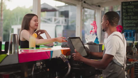 la dama paga la bebida con el teléfono en la terminal de café pos. el barman negro coquetea con una atractiva cliente femenina ofreciendo descuento por el pedido. la mujer compra un cóctel