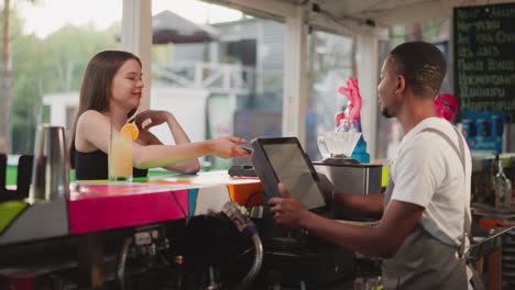 lady pays for drink with phone on cafe pos terminal. black barkeeper flirts with attractive female customer offering discount for order. woman buys cocktail