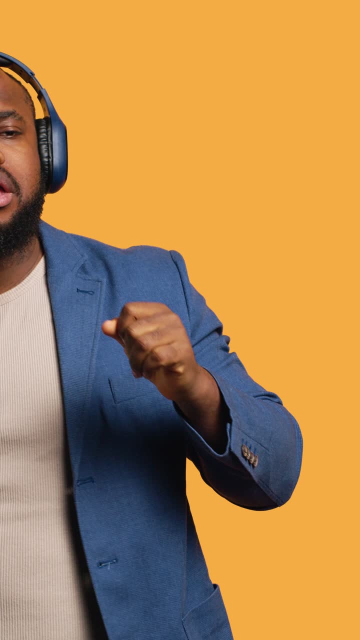 Vertical video Carefree man listening energic music, dancing on rhythm, studio background