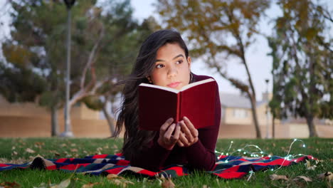 una mujer joven leyendo las páginas de un libro de cuentos o una novela al aire libre con hojas de otoño en cámara lenta