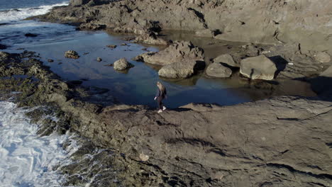 aerial shot with tracking of a young woman who walks between the natural pools and where the waves of the sea can be appreciated