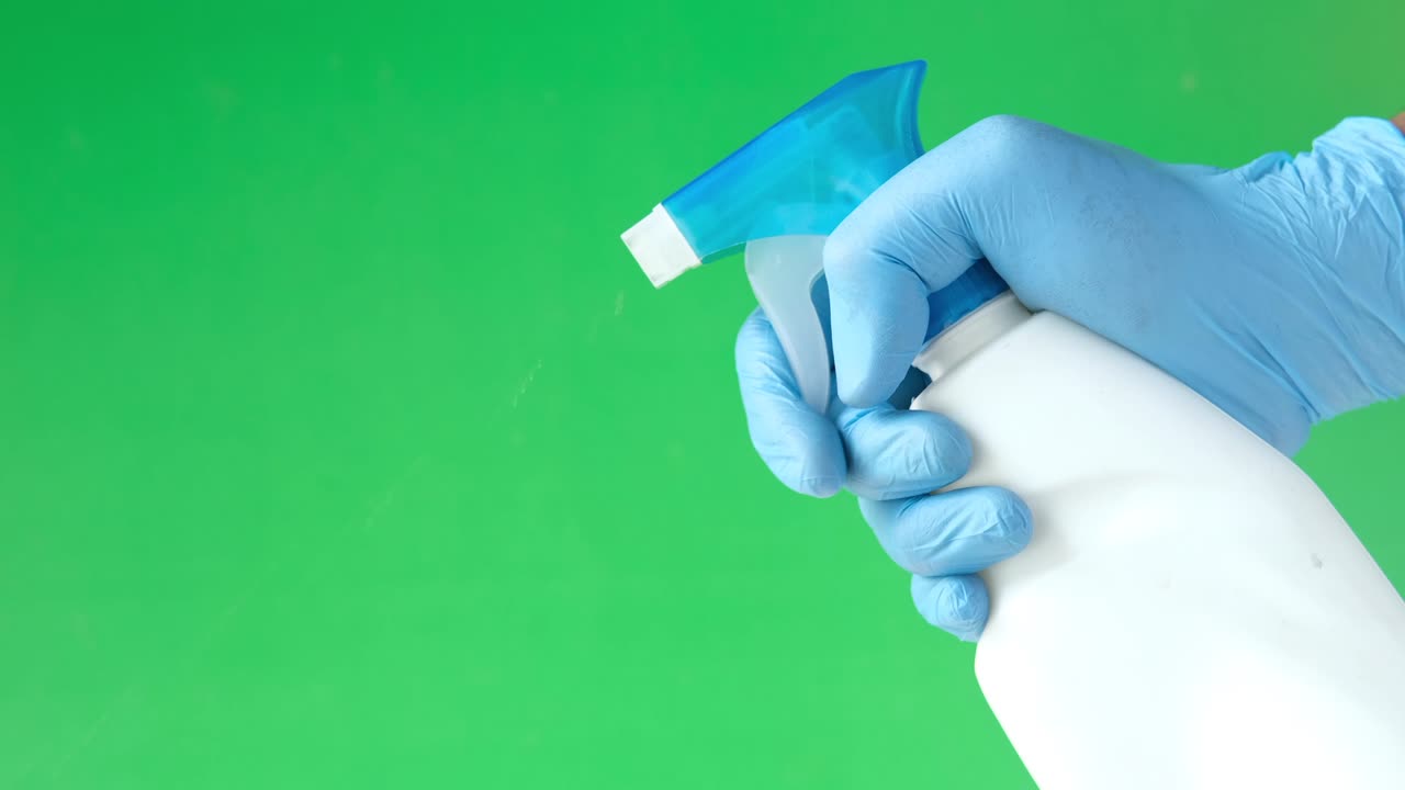mano con guantes de goma azules sosteniendo spray contra un fondo verde