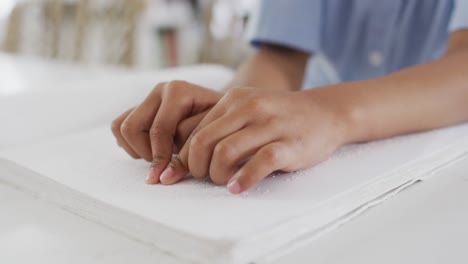 close up of african american boy sitting at table and reading braille