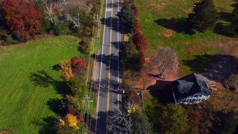 a high angle aerial view over a country road with colorful trees around on a sunny day in autumn