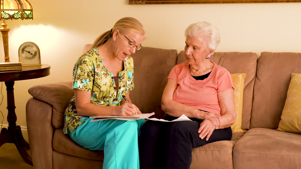 Front view of home healthcare nurse and elderly woman sitting on a couch looking over paperwork