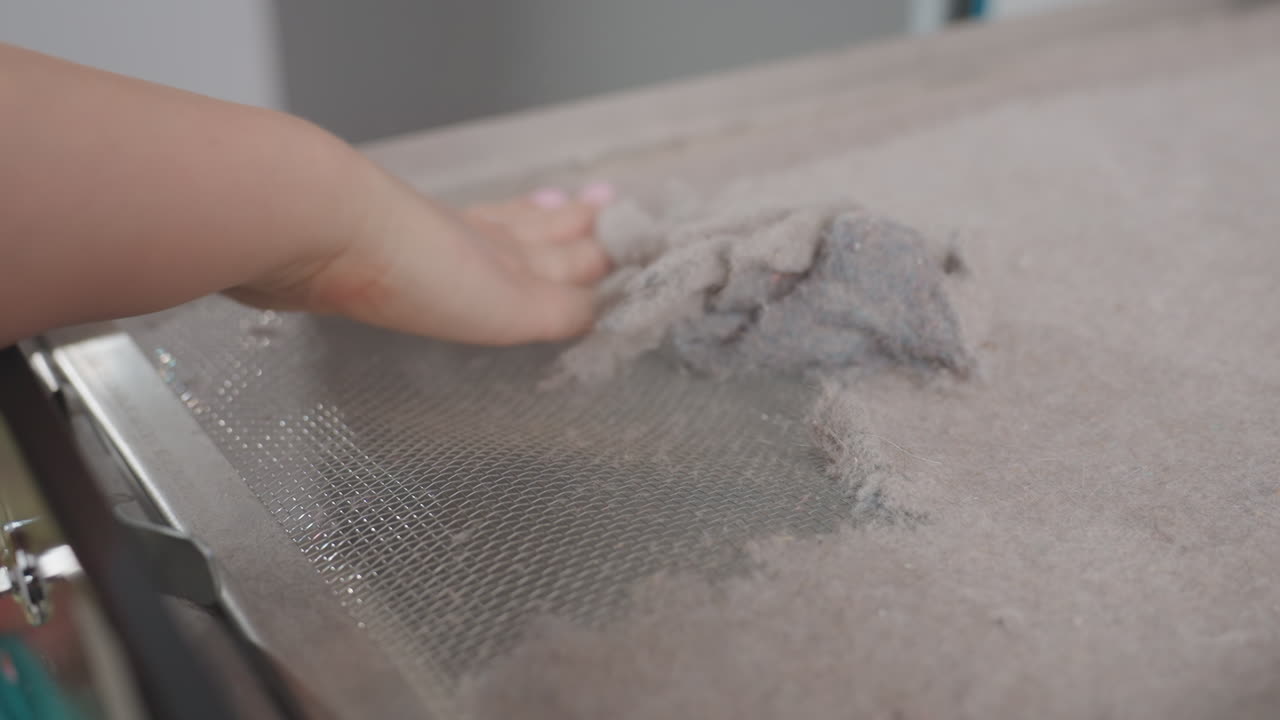 Close up view woman hand removing dirt and lint from washer filter mesh, ensuring equipment hygiene and effective maintenance inside laundromat environment for smooth operation of industrial machine