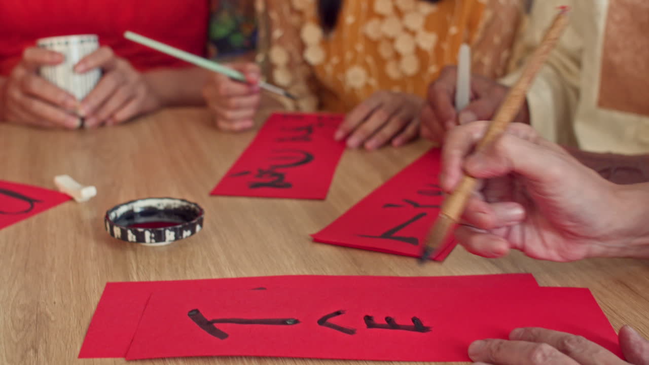 Hands of People Writing Calligraphy on Red Paper