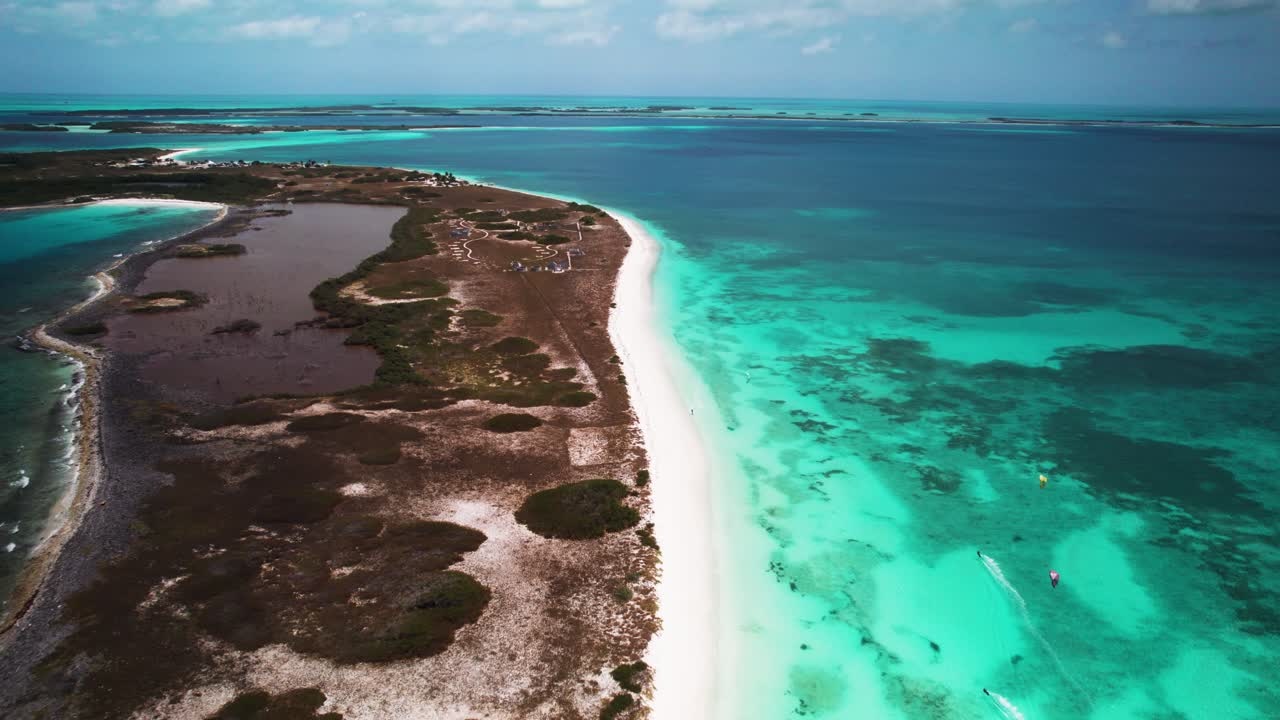 Turquoise waters meet white sands on a remote island coastline under a sunny sky