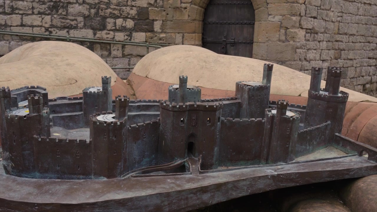 Inquadratura stabile di una dettagliata scultura in metallo del Castello di Caernarfon, esposta all'interno del castello, con un'illuminazione soffusa che evidenzia l'intricata maestria artigianale, le superfici riflettenti e l'architettura storica.