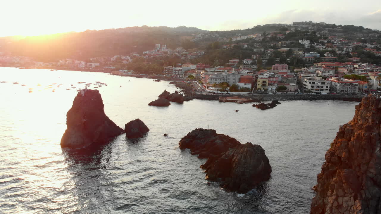 ciudad costera con pequeñas islas rocosas, puesta de sol sobre colinas a lo lejos, vista aérea