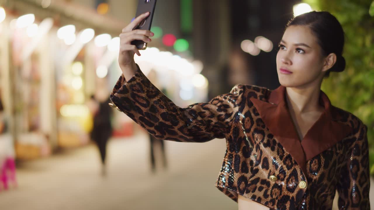 Sunningly seductive Asian girl wearing leopard print takes a selfie with her smartphone then posts it on social media