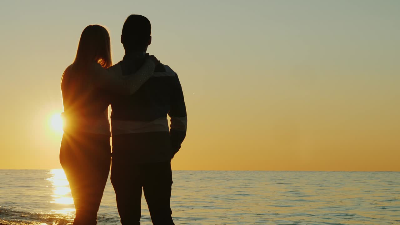 젊은 커플이 안고 해가 지는 것을 함께 감상하는 실루