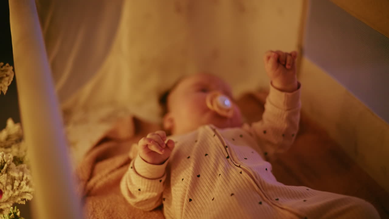 Primo piano di un bambino con un ciuccio illuminato da calde luci natalizie, che crea un’atmosfera festosa e toccante