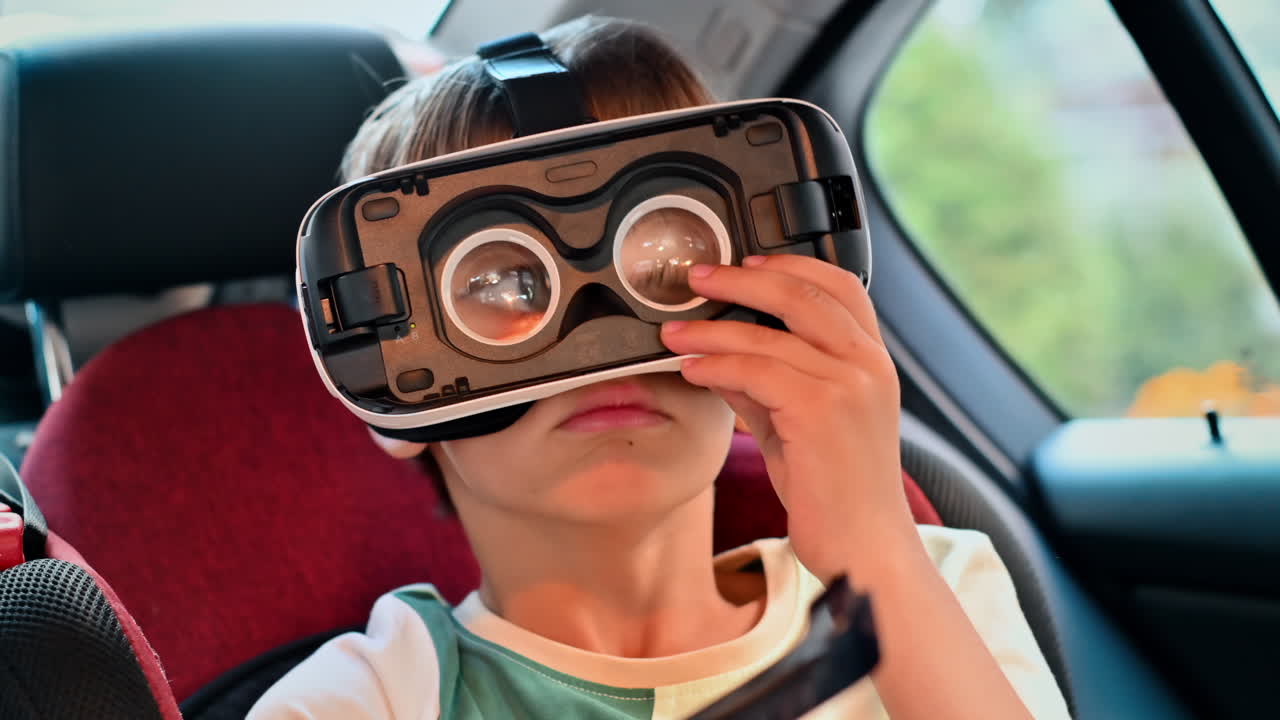 Boy sitting in the car in VR glasses without front cover in child safety seat and pointing with hand. Slow motion