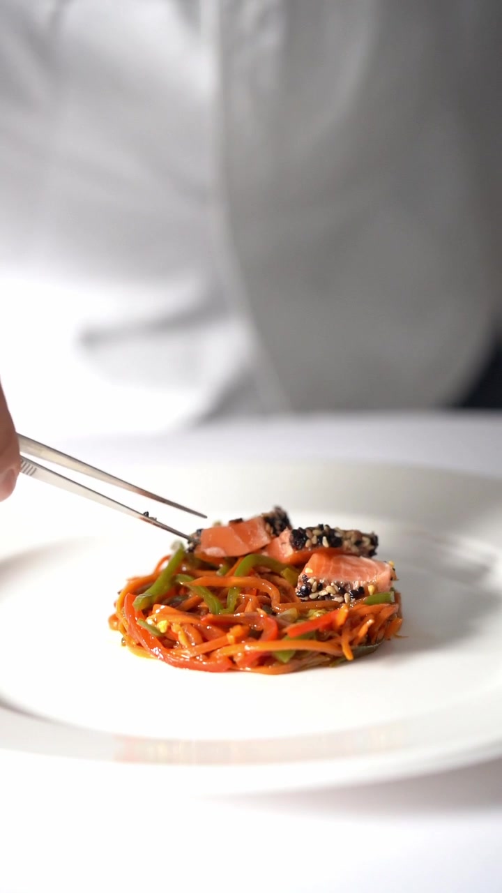 Chief plating a gourmet dish with vegetables and meat in a minimalist style, close up shot, insert shot