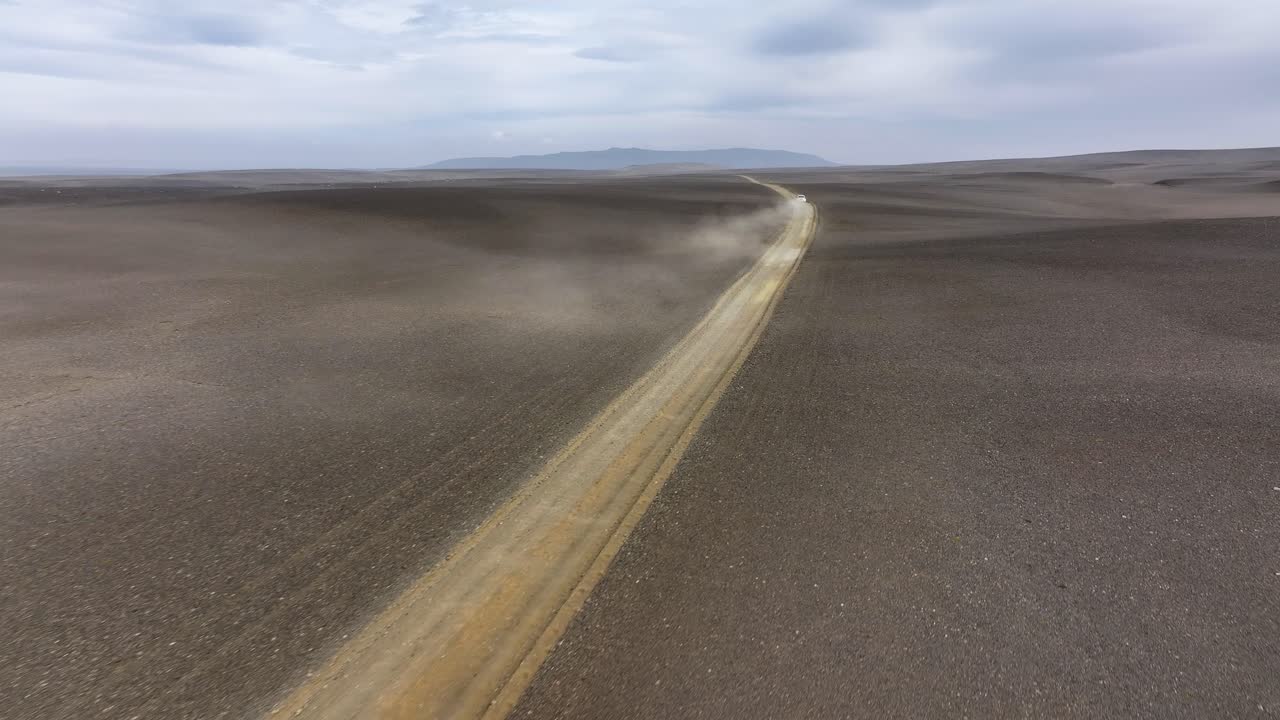 A rugged SUV drives along a dusty backcountry road in Iceland, surrounded by flat barren volcanic landscapes and the raw beauty of the Highlands