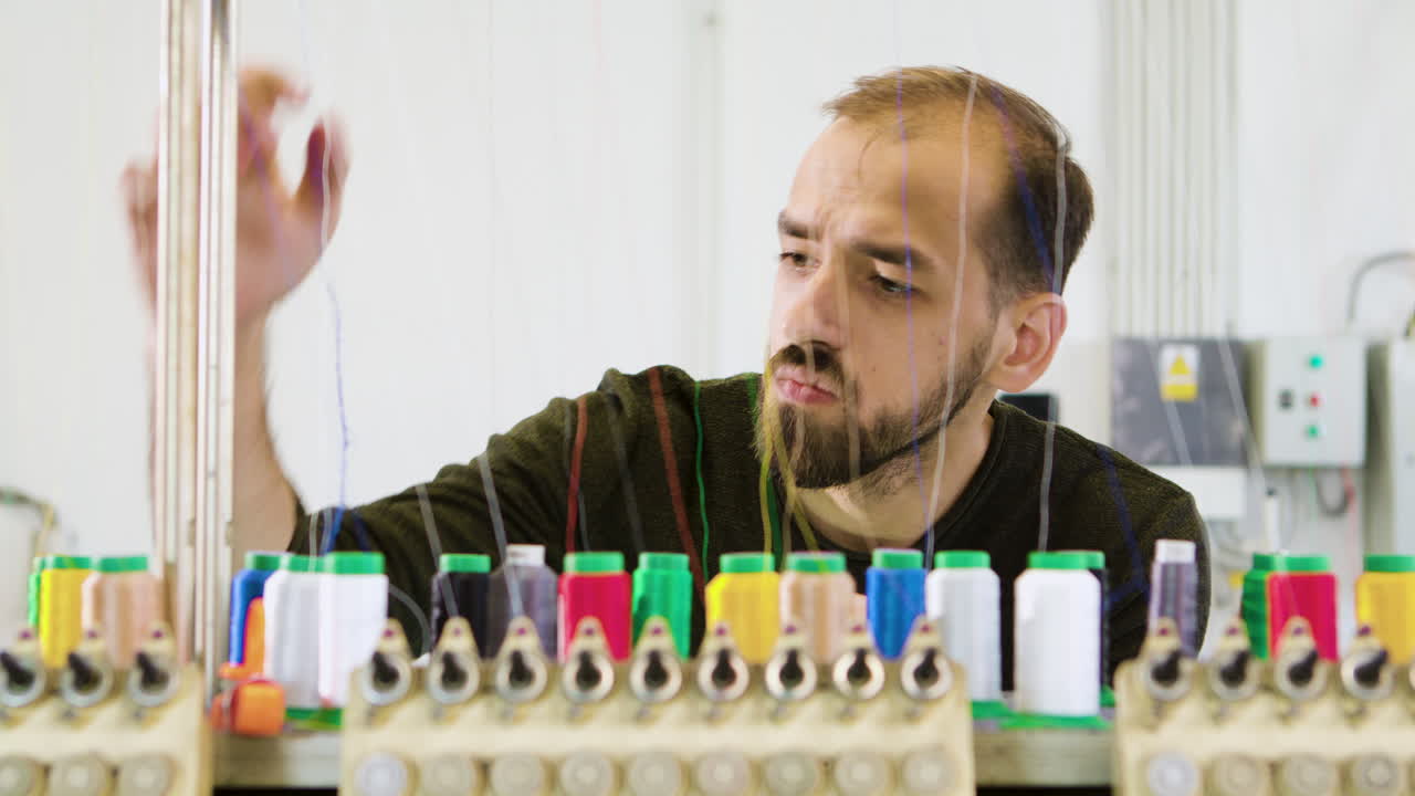 Giovane uomo in una moderna fabbrica di tessuti che controlla i macchinari per cucire.