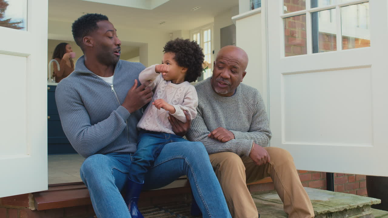 familia masculina de varias generaciones sentada en el escalón en casa jugando y divirtiéndose juntos