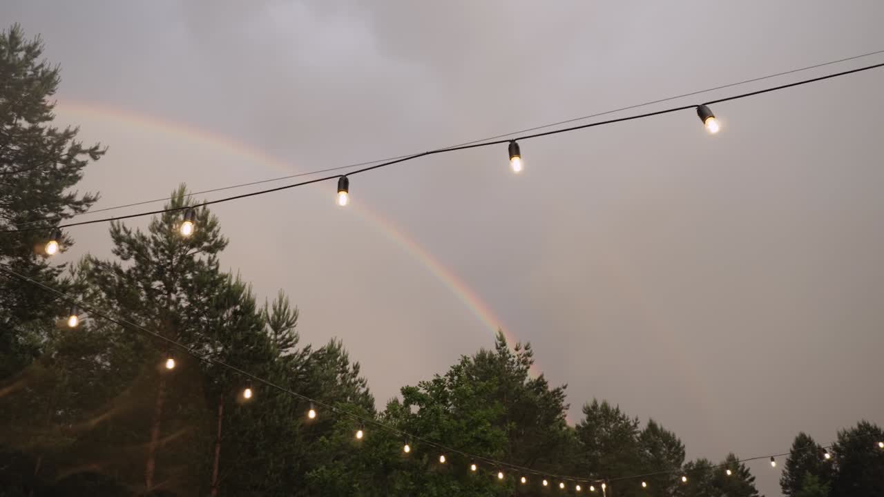 un arco iris brillante sobre un bosque verde en un cielo nublado con una guirlanda de bombillas de vidrio.