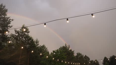 bright rainbow over green forest in overcast sky with garland of glass bulbs.