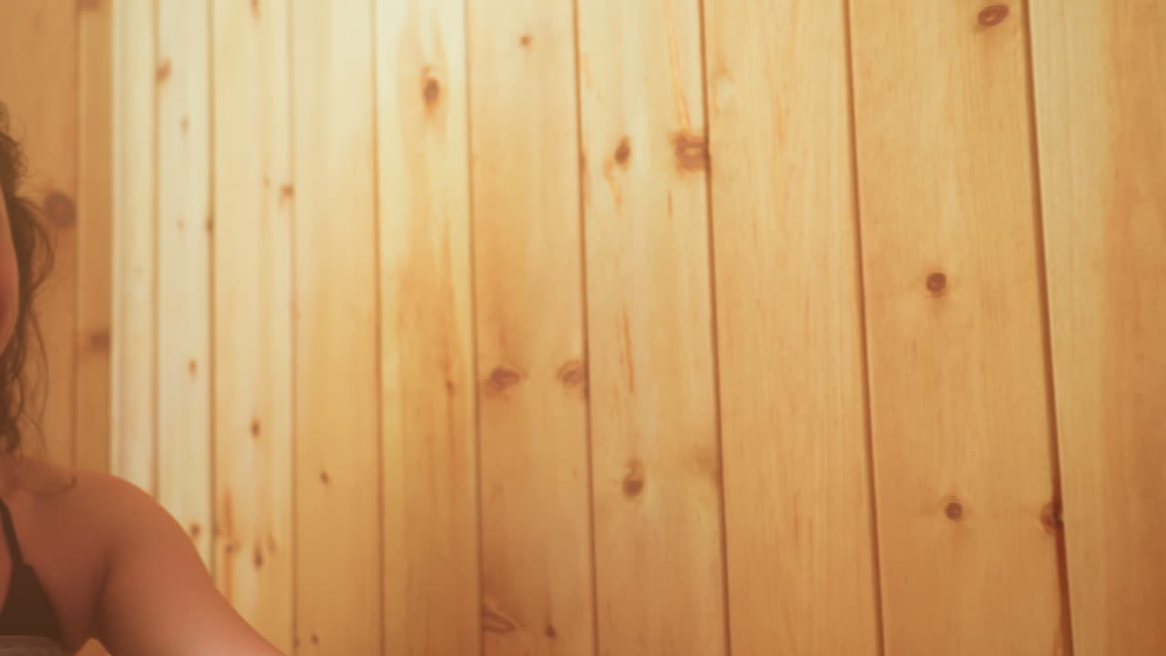 Close up of sisters leaning against wood paneled wall, one gazing lovingly at sibling while soft backlight creates warm haze over wet curls, capturing tender connection
