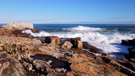 Waves-crashing-into-rocky-shore-creates-frothing-whitewash,-dramatic-dolly-shot