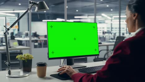 mujer de negocios caucásica exitosa sentada en el escritorio trabajando en una computadora portátil de pantalla verde en la oficina. hermosa mujer de negocios usando una pantalla de llave cromada. sobre el hombro disparo estático
