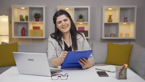 una mujer trabajadora de oficina en el hogar sonriendo a la cámara mirando el papeleo.