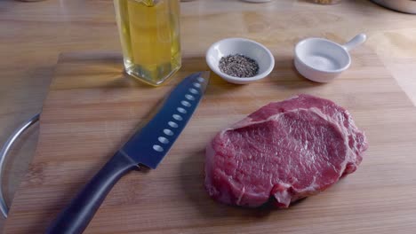 slow motion slider shot of a raw ribeye steak on a wooden cutting board prior to cooking