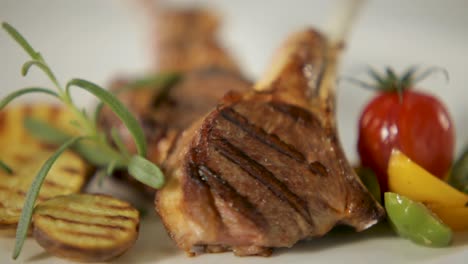 chuletas de cordero a la parrilla con romero, centrarse en la carne con verduras borrosas en el fondo, cocina de alta gama