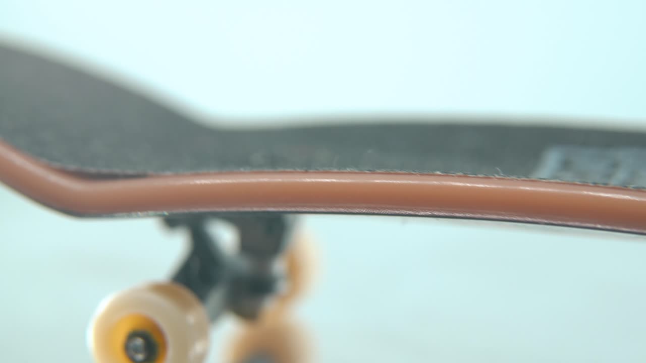 A hyper macro detailed shot of a mini skateboard, tiny white wheels, fingerboard on a 360 rotating stand, shiny mirror reflection, professional lighting, cinematic 4K video tilt up