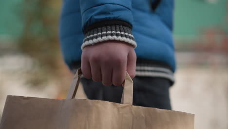 close-up of person in blue clothing holding shopping bag, with blurred autumn foliage and residential background, capturing a moment of simplicity and vibrant seasonal atmosphere