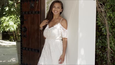 atractiva joven morena en vestido blanco de pie junto a la pared