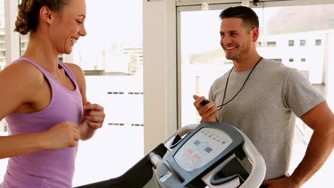 Fit-woman-running-on-treadmill-with-trainer-timing-her