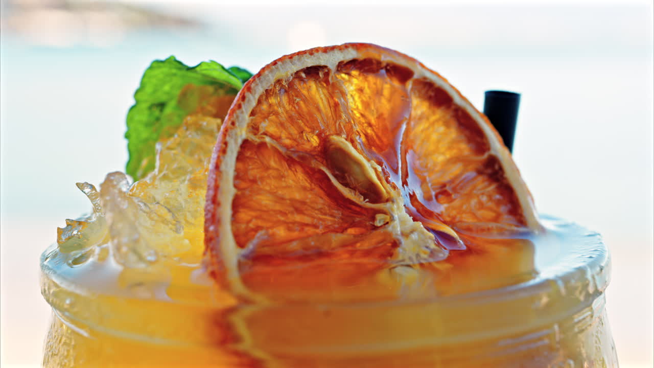 Close up of an orange cocktail on a table with a blurred view of the sea on the background