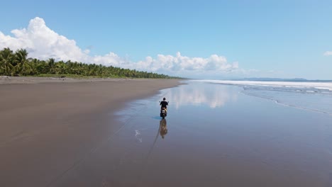 Mann-Fährt-Motorrad-über-Einen-Nassen,-Himmlischen-Strand,-Wo-Palmen-Auf-Den-Südpazifik-Treffen