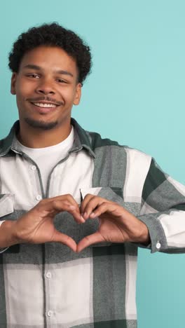 happy young man gesturing heart on blue background