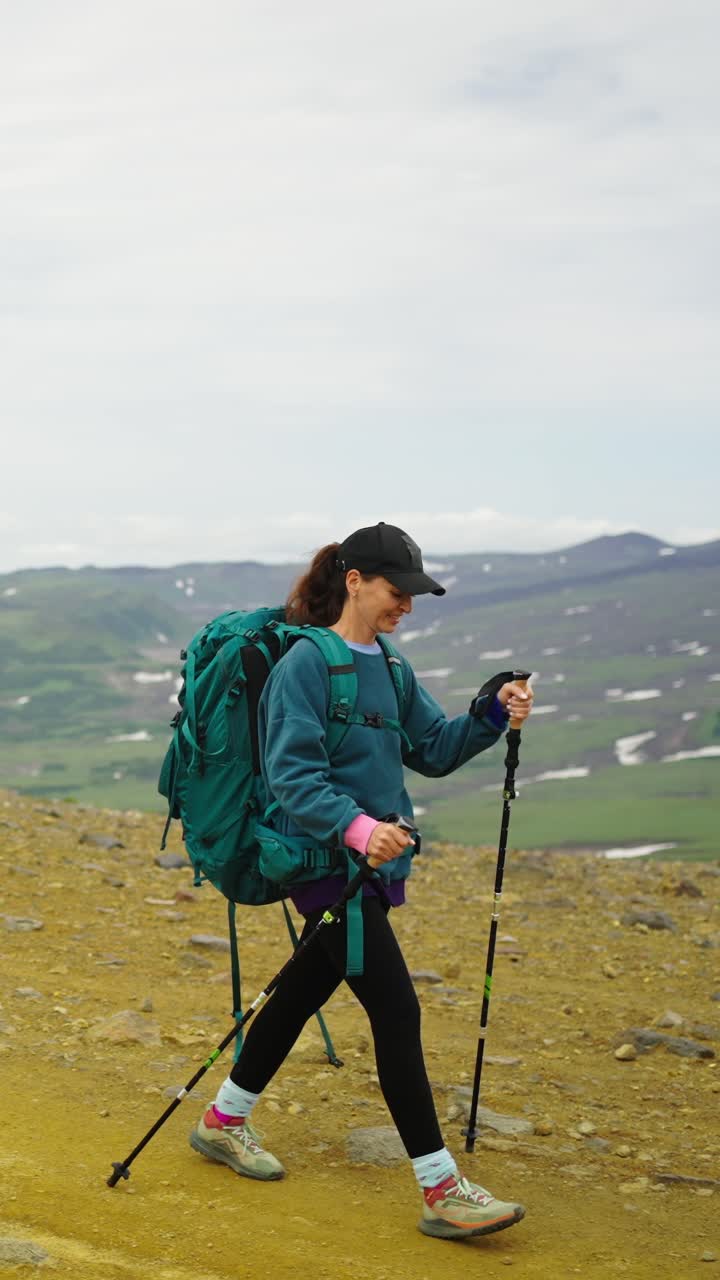 Donna felice che fa trekking con zaino e bastoncini in un paesaggio montano