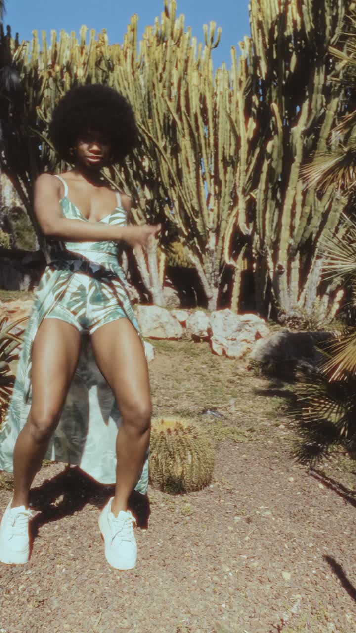 Giovane donna energica che balla in un giardino tropicale di cactus