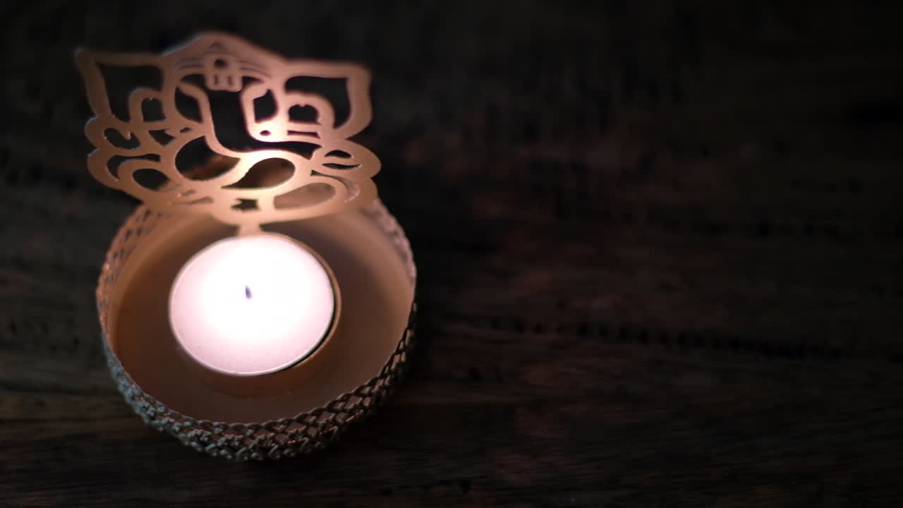 Primo piano con panoramica a sinistra su una candela da tè in cera davanti a una sagoma dorata di Lord Ganesha durante il Diwali, festa delle luci, celebrazioni di culto al buio per mostrare la luce.