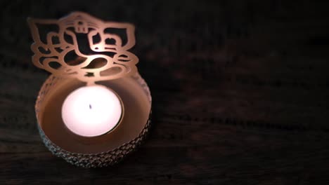 close-up panning left to a wax tea candle in front of lord ganesha golden cutout during diwali, festival of lights, worship celebrations in dark to show the light.