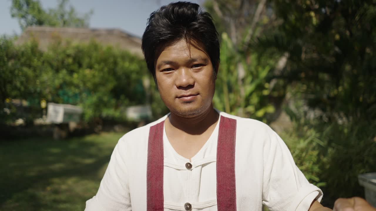 A man in traditional attire, potentially a beekeeper, showing a beehive frame full of bees