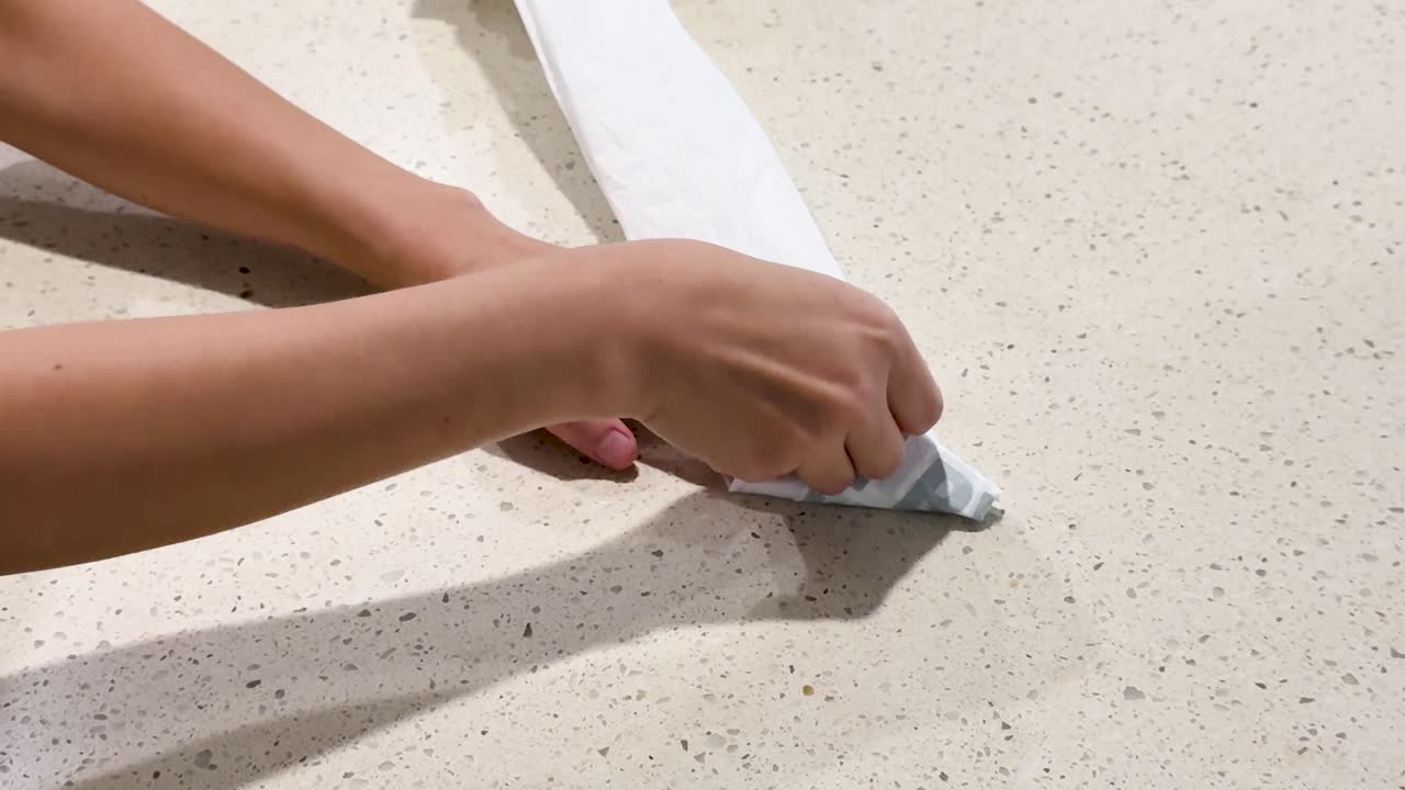 Hands skillfully fold a reusable plastic bag on a countertop under bright lighting, demonstrating efficient storage techniques