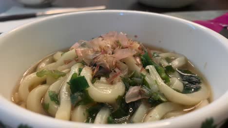 moviendo hojuelas de pescado sobre un plato caliente de fideos udon
