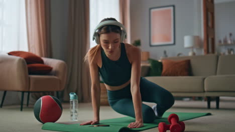 sportswoman stretching body home at sport mat wearing wireless headphones.