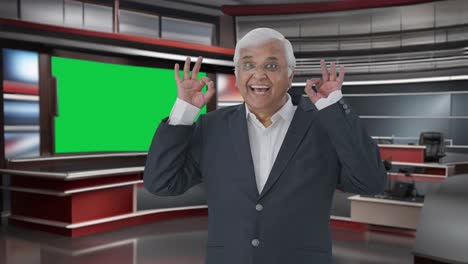 Happy-Indian-senior-journalist-pointing-at-green-screen-showing-okay-sign