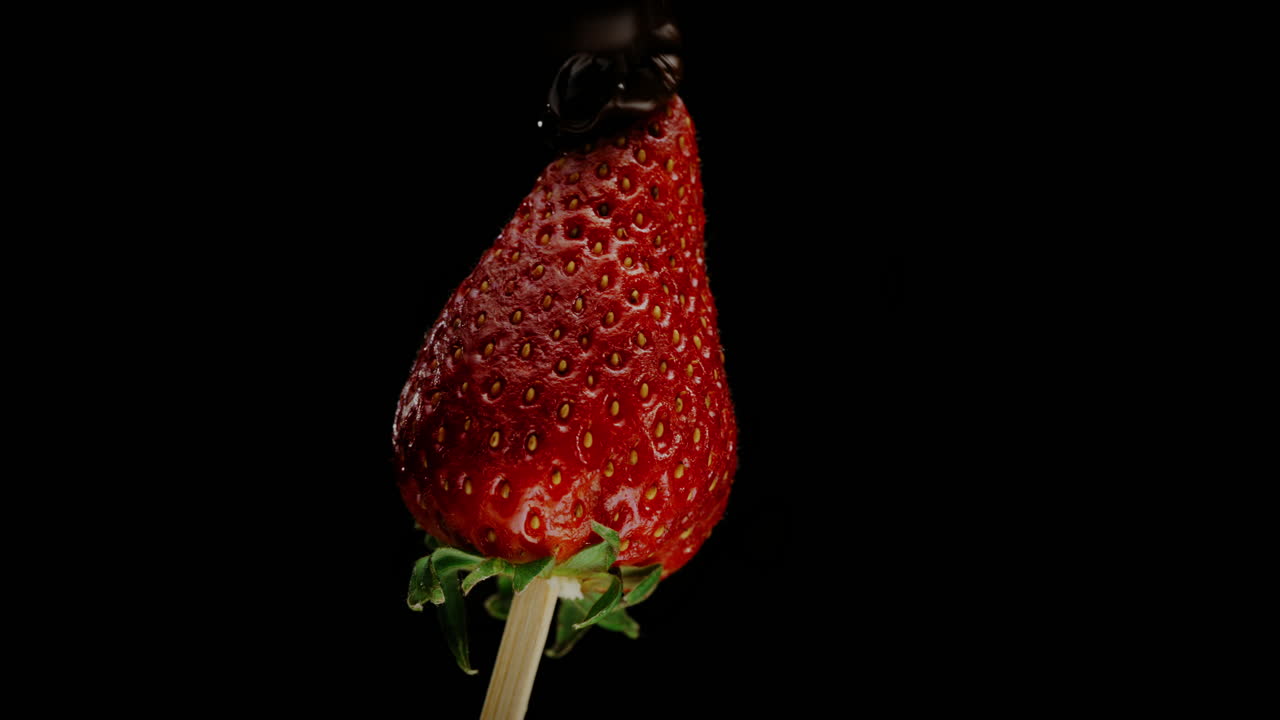 el chocolate con leche espeso se rocía sobre una jugosa fresa roja, macro, rotando